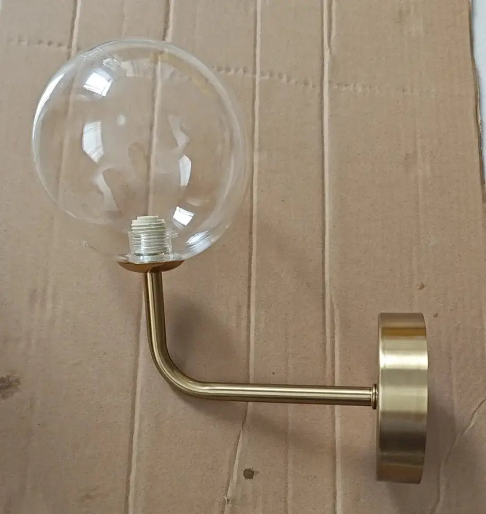 A sleek retro brass wall lamp with a curved arm and clear decorbites glass ball for bedroom lighting