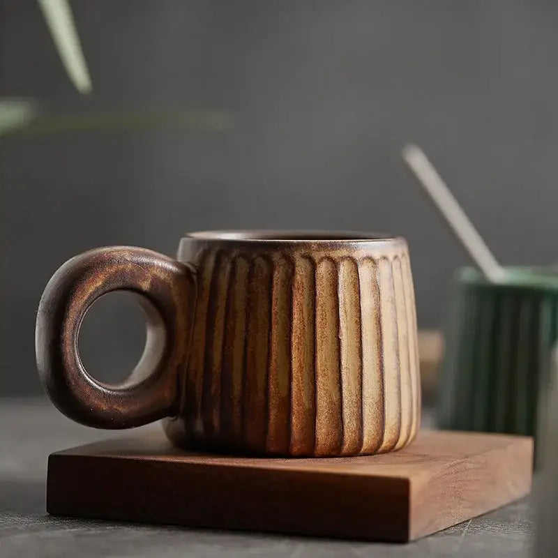 A rustic brown handmade nordic ceramic mug with vertical ridges and ring handle on a wooden coaster by decorbites