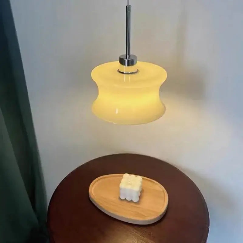 A warm yellowish retro cream decorbites glass chandelier with chrome stem and curved glass shade above wooden table