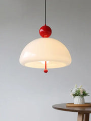 A retro cream glass pendant light with glossy red accents suspended by a black cord above a wooden table