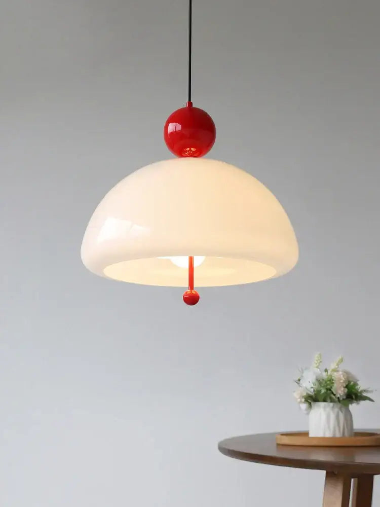 A retro cream glass pendant light with glossy red accents suspended by a black cord above a wooden table