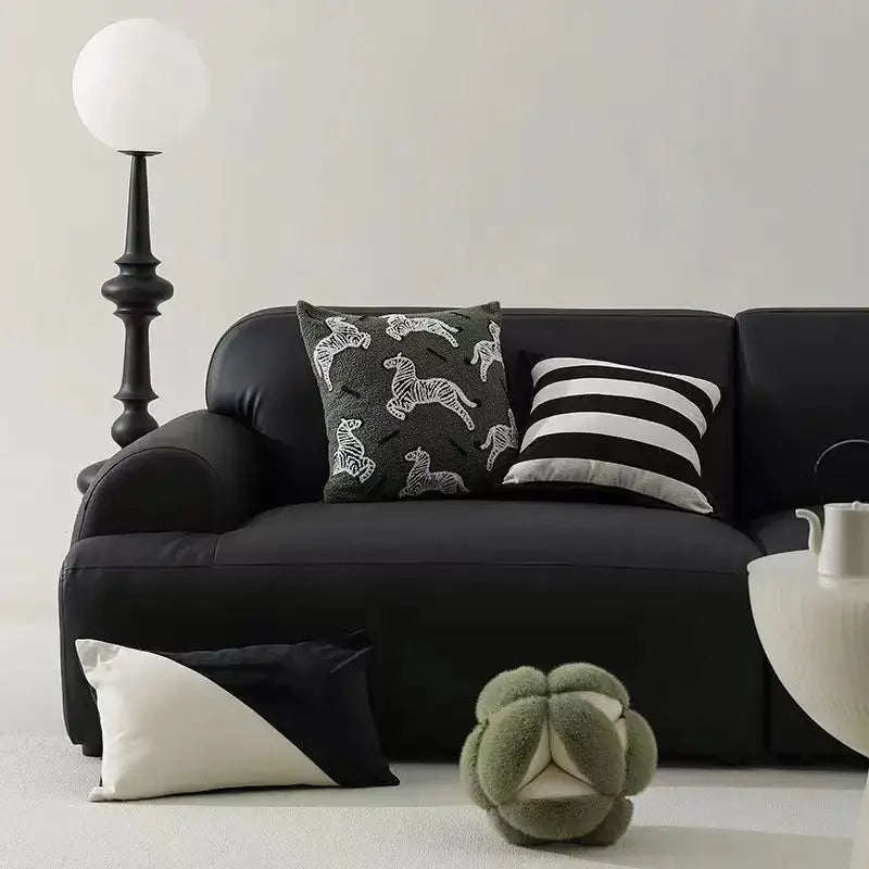 Black leather sofa with two embroidered jacquard luxury pillow covers and a plush green footstool in bedroom setting