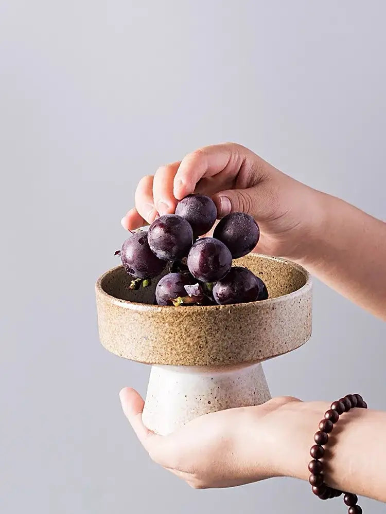 A retro floral ceramic footed bowl with speckled beige glaze holds dark purple grapes by decorbites handmade