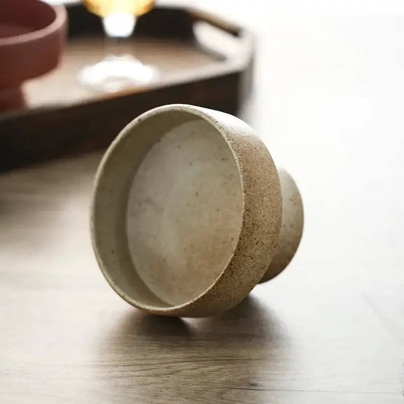 A retro floral ceramic beige speckled handmade cup with flared rim resting on its side by decorbites