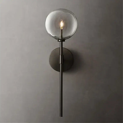A sleek matte black wall sconce with a clear glass ball globe and illuminated bulb for living room lighting