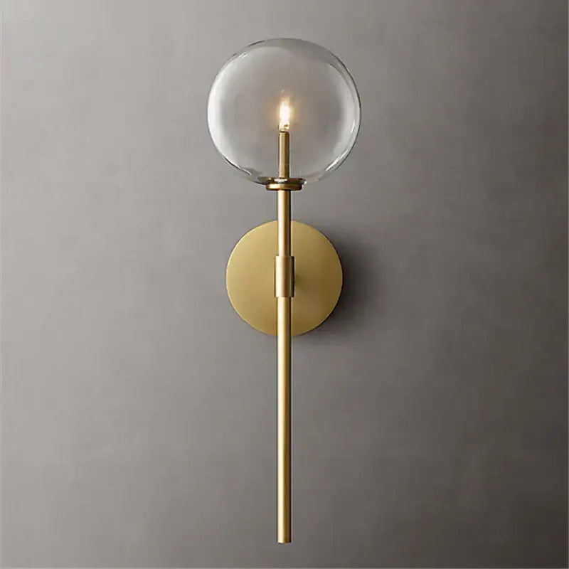 Retro gold wall sconce with a clear glass ball and slender cylindrical stem for living room lighting