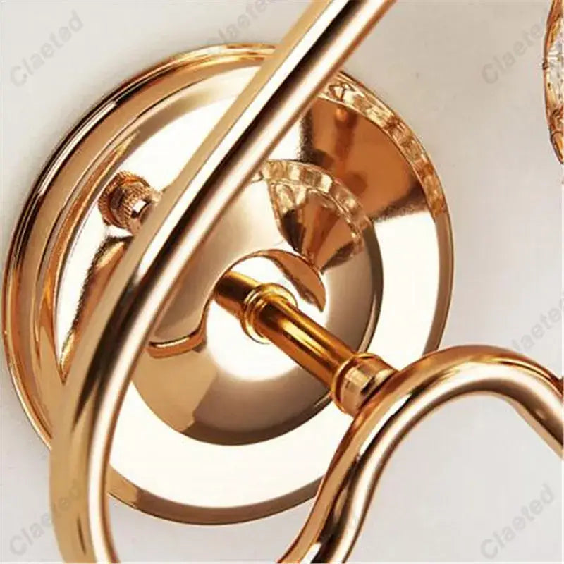 Gold-toned metal retro industrial wall lamp sconce with ornate curved arms and polished reflective surfaces for bedroom