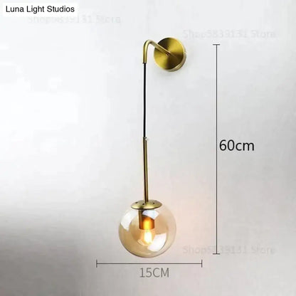 A modern brass-finished wall lamp with a spherical amber glass globe and curved arm, ideal for bedroom lighting