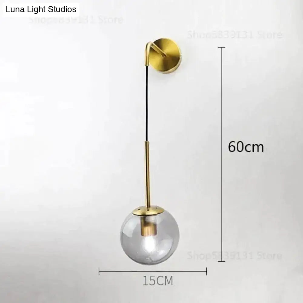A gold-toned nordic retro modern wall lamp with clear glass smoked globe and slender metallic stem for bedroom lighting