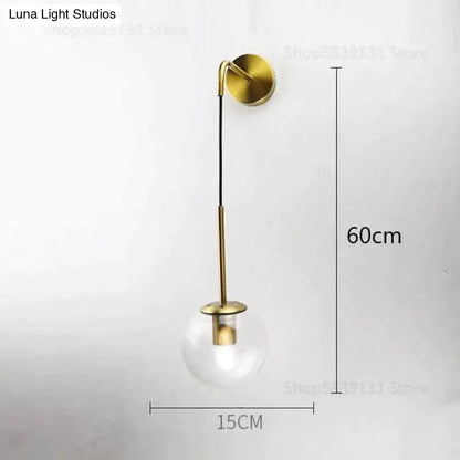 A sleek brass-finished nordic retro modern wall lamp with minimalist curved arm and clear glass smoked globe bulb