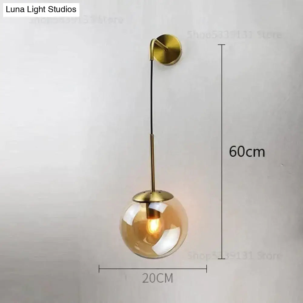 A sleek brass-finished nordic retro modern wall lamp with a spherical amber glass globe for bedroom lighting
