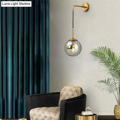 A sleek retro modern glass smoked globe wall lamp with gold-toned metal arm for bedroom lighting