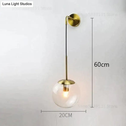 A sleek brass-finished retro modern glass wall lamp with clear globe and slender stem for bedroom lighting