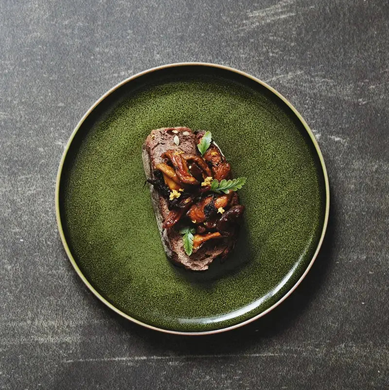 A rustic green ceramic dinner plate with textured speckled glaze and subtle gold rim for dining room use