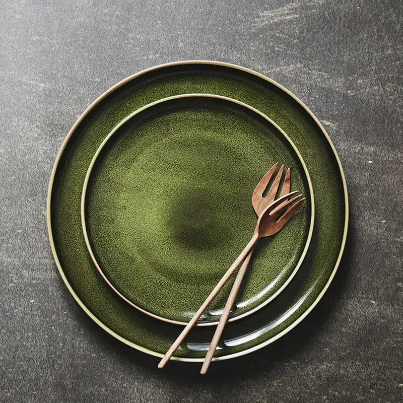 Set of two retro olive green ceramic dinner plates with matte finish and gold rim accompanied by wooden utensils