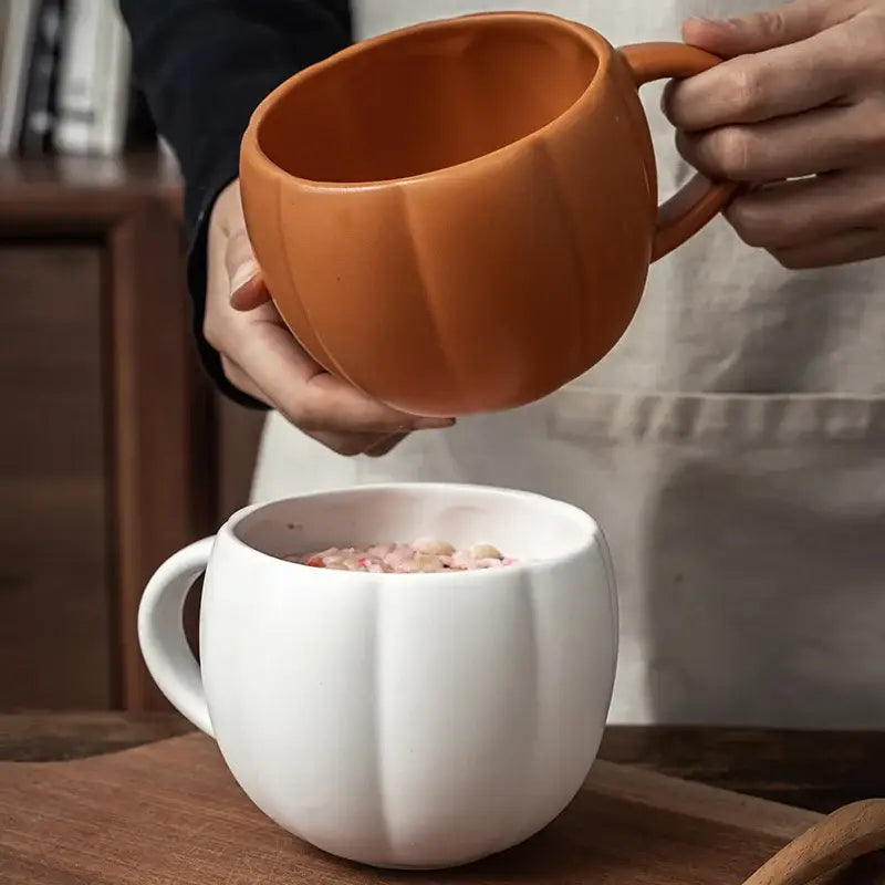 Orange halloween pumpkin ceramic mug with retro enamel handle being poured into white pumpkin ceramic mug