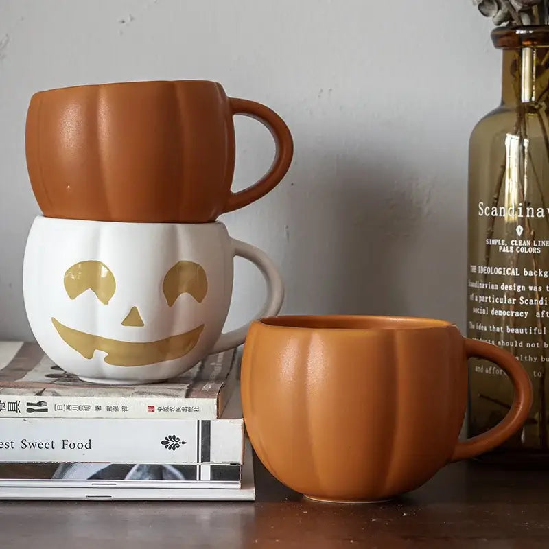 Two retro orange pumpkin ceramic mugs with white base, gold jack o lantern face, and enamel handle for halloween use