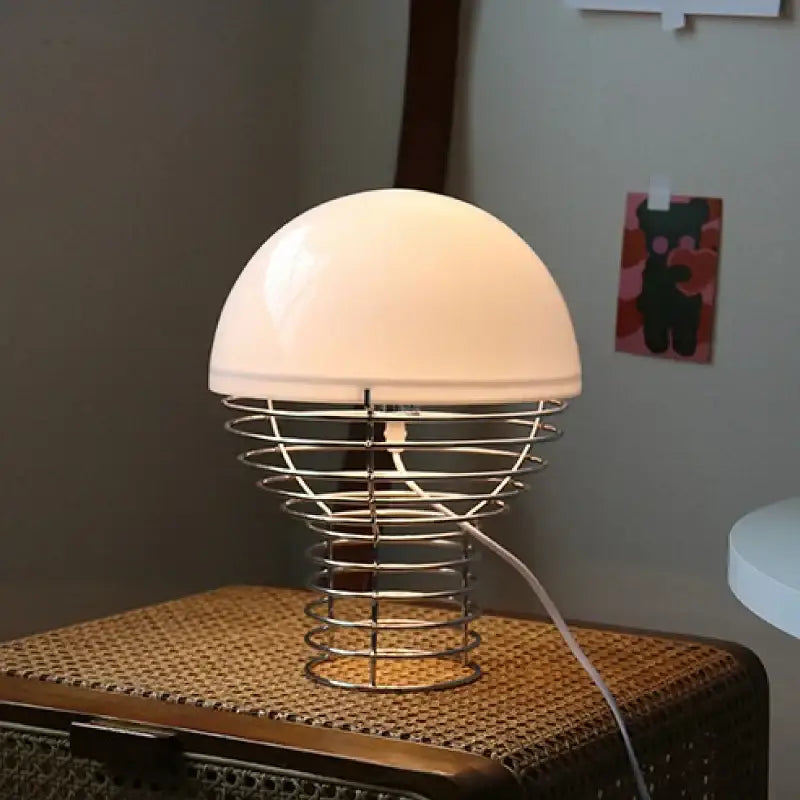 A sleek retro red glass table lamp with a glossy white acrylic shade and chrome wireframe base for bedroom use