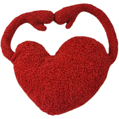 A plush vibrant red heart-shaped handbag with soft textured surface and integrated handles resembling hands holding each other