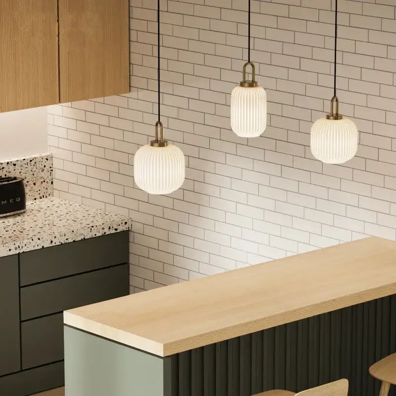 Three elegant white ribbed glass pendant lights with brass accents hang above a modern kitchen counter