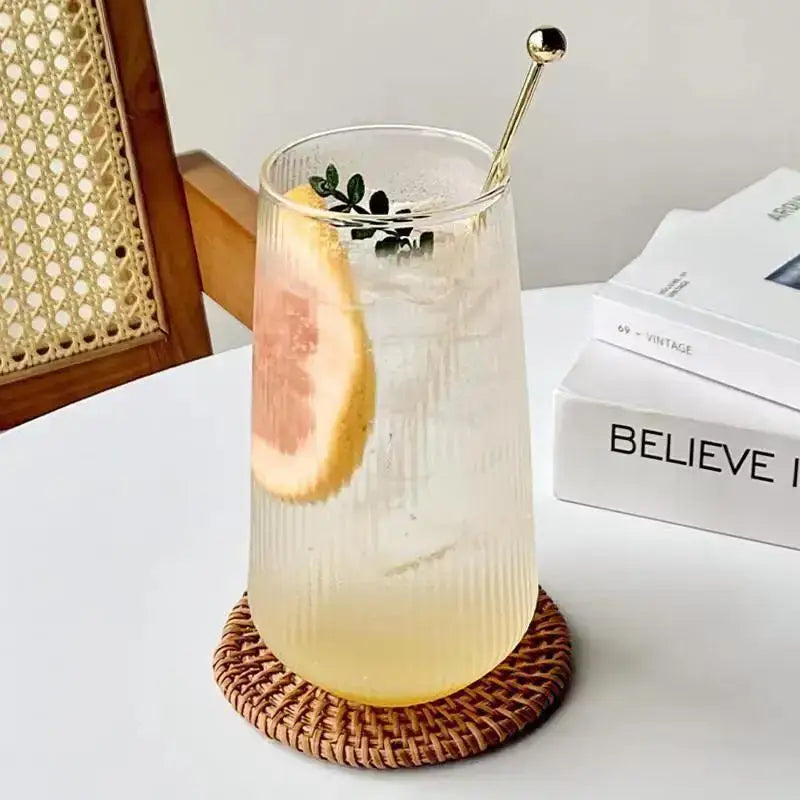 Tall clear retro ribbed glass coffee cup filled with pale yellow beverage garnished with grapefruit slice and green leaves