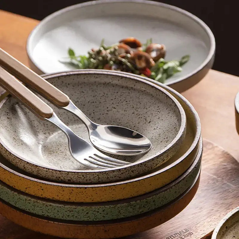 Stack of retro speckled beige ceramic round plates with wooden-handled silverware in decorbites ceramic round set
