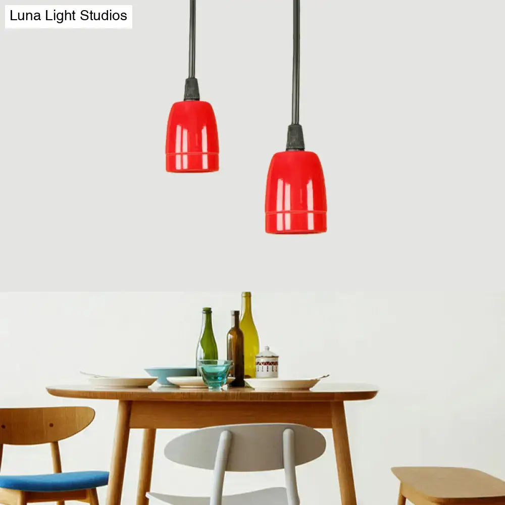 Two vibrant red ceramic pendant lights with black cords hang above a wooden table in black red ceramic finish
