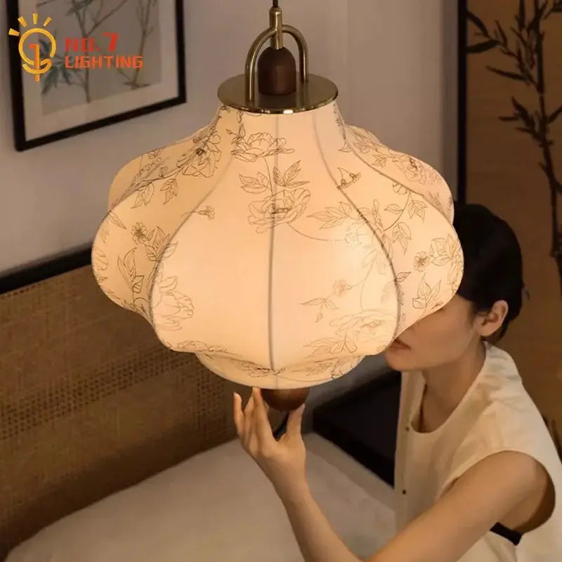 A cream fabric pendant light with gold floral embroidery hanging from a brass fixture retro pendant lights decorbites wabi-sabi