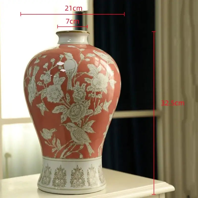 A coral-red ceramic vase with white floral and bird motifs and a silver-embossed base for living room decor