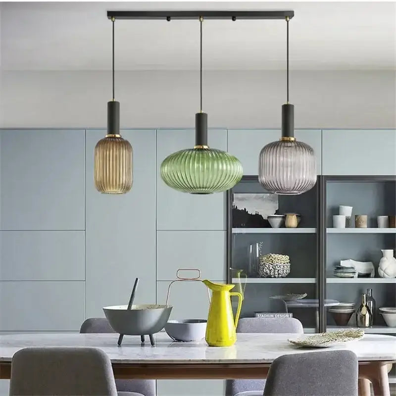 Three modern pendant lights with ribbed amber green and grayish blue glass shades hang above a dining table