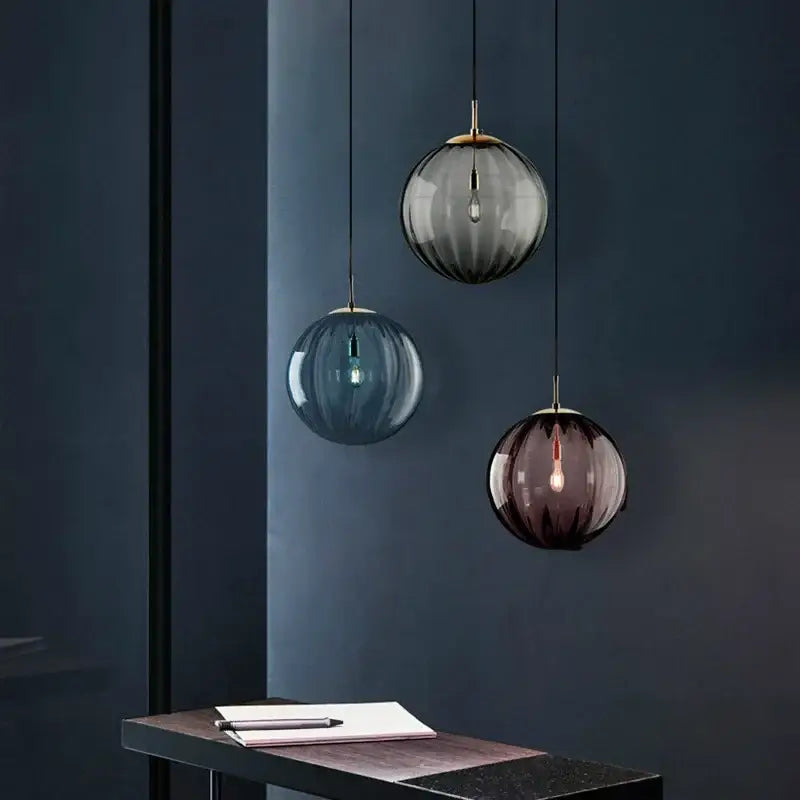 Three ribbed colorful glass ball pendant lights in gray blue and purple hang from black cords as decorbites pendant lamps for living room decor