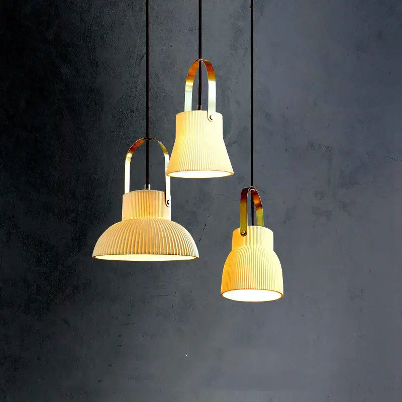 Three modern ribbed cream ceramic led pendant lights with brass handles hang against a dark wall decorbites ceramic led