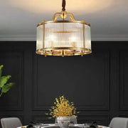 A gold-toned decorbites glass chandelier with vertical ribbed panels suspended by a twisted brown cord