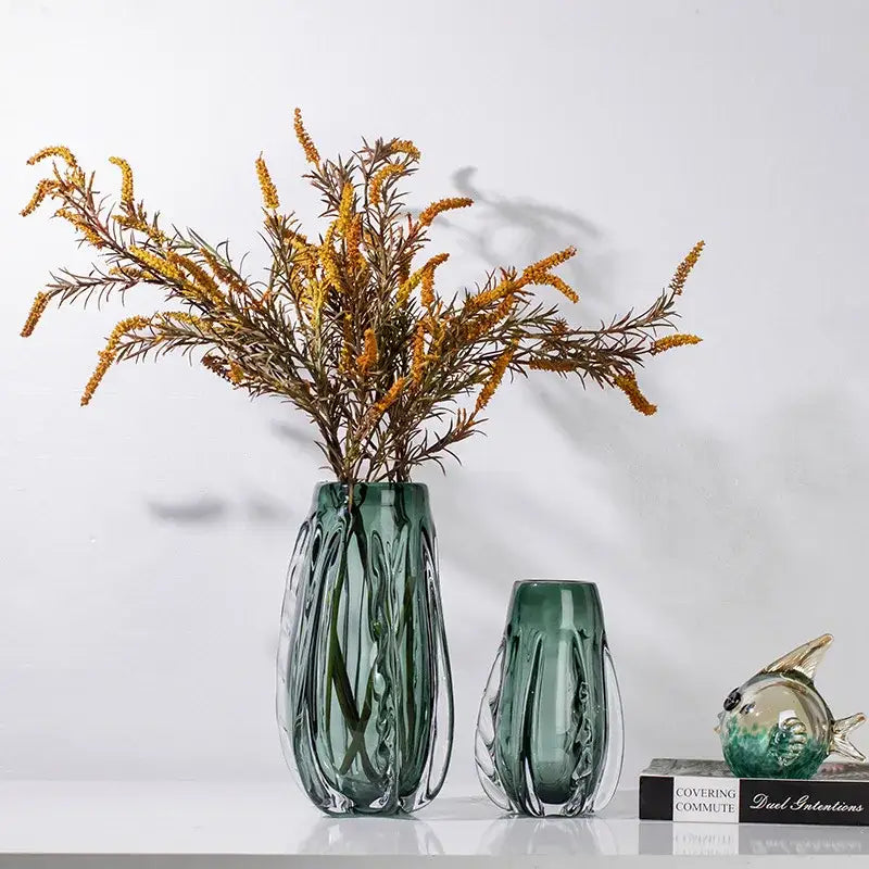A tall ribbed emerald green decorbites crystal vase holding golden-yellow dried flowers for living room decor