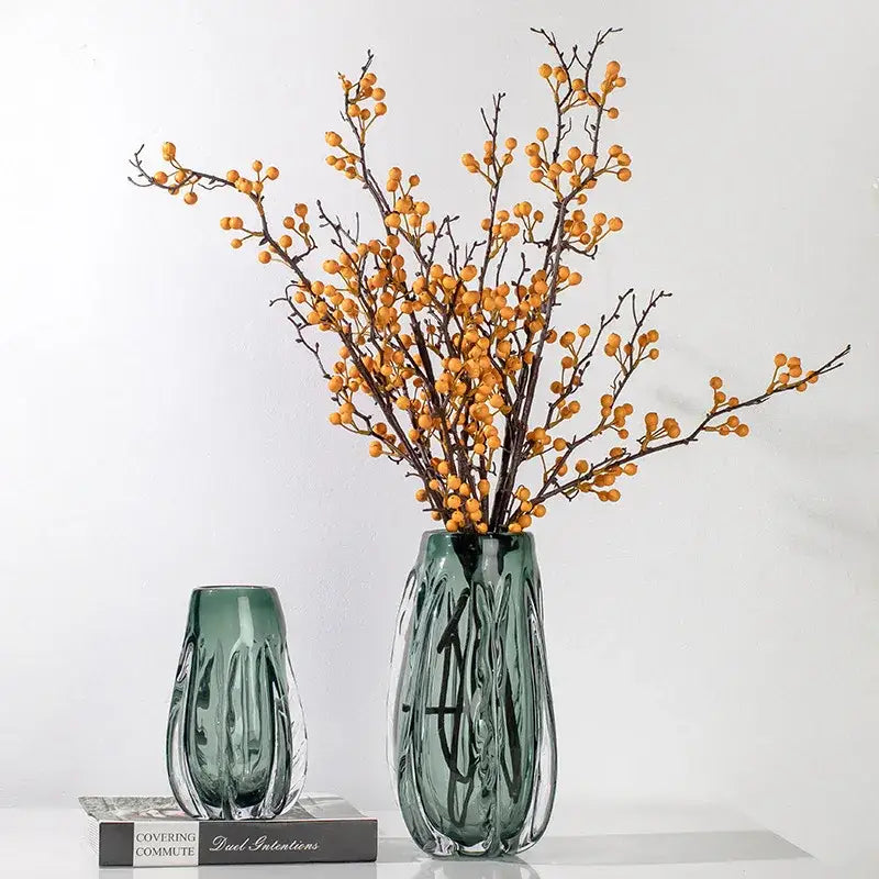 A tall ribbed emerald green decorbites crystal vase with modern design holds orange berry branches for living room decor