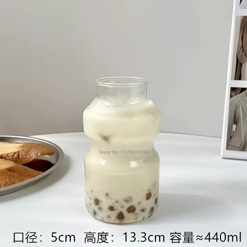 A clear ribbed frosted borosilicate glass cup filled with creamy milk tea and black tapioca pearls