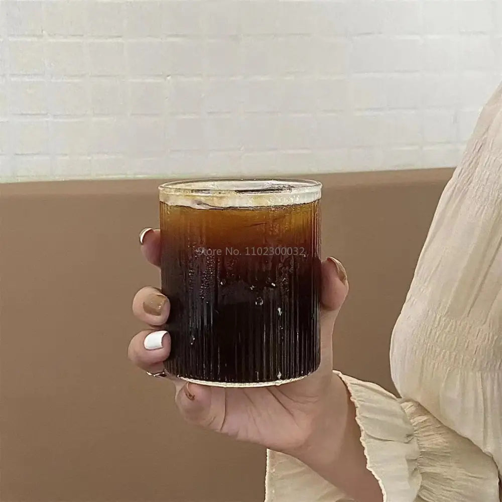 A clear ribbed glass tumbler filled with dark iced coffee from a ribbed frosted and clear glass coffee cups set of 6