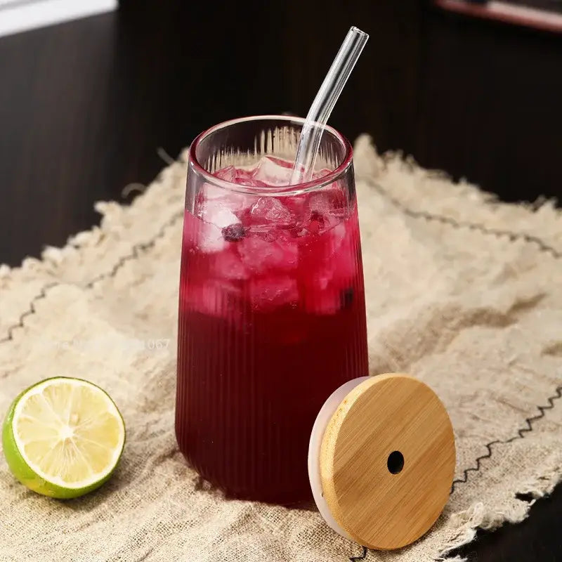 Tall ribbed glass cup with vibrant red beverage and ice cubes from glass cup set with bamboo lid and straw for dining
