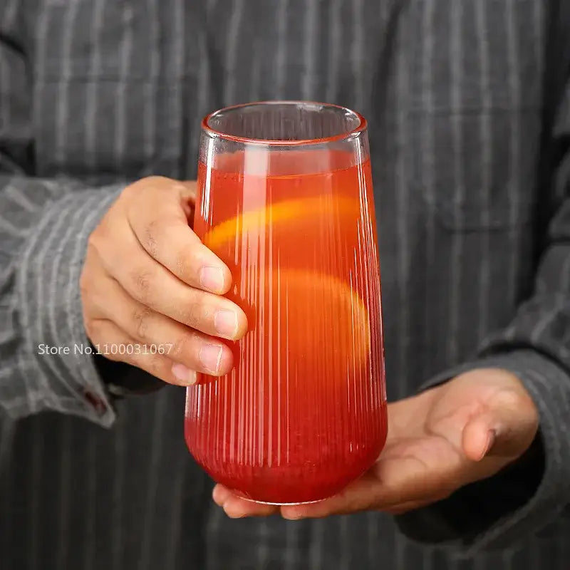 A ribbed glass cup from the glass cup set holds a vibrant red beverage with orange slices for kitchen dining