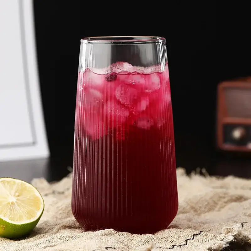Tall clear glass cup with vertical ridges filled with red beverage and ice from ribbed glass cup set with bamboo lid and straw