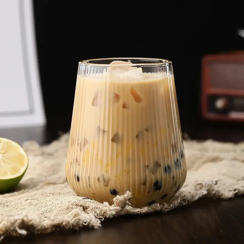 A clear ribbed glass cup filled with creamy iced coffee and black tapioca pearls from a glass cup set with bamboo lid and straw