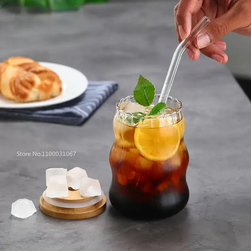 A clear ribbed glass cup from decorbites glass cup set filled with iced coffee garnished with lemon slices and mint leaves