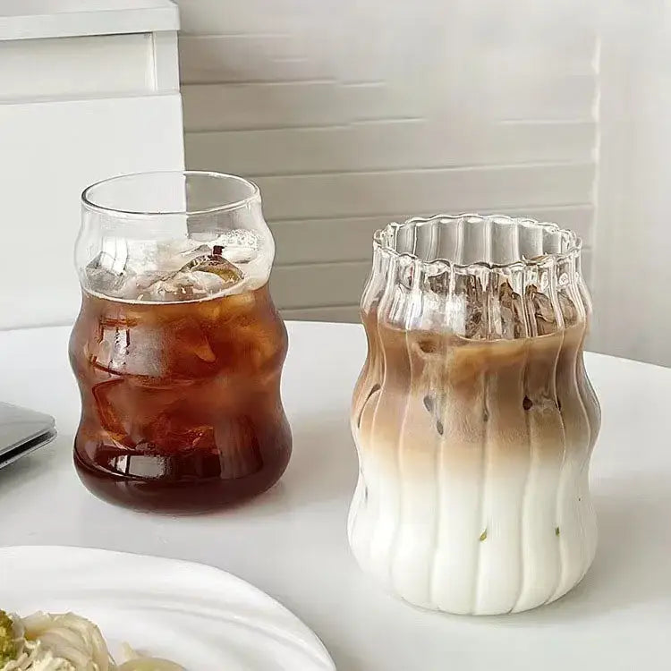 Two ribbed glass cups with wavy contours filled with iced coffee and layered drink featuring lip straw decorbites glass cup