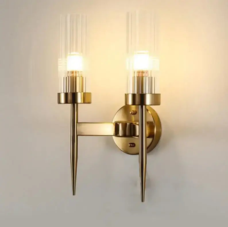 Brass-finished gold led wall light with two clear ribbed glass candle shades and slender pointed arms for bedroom decorbites gold led