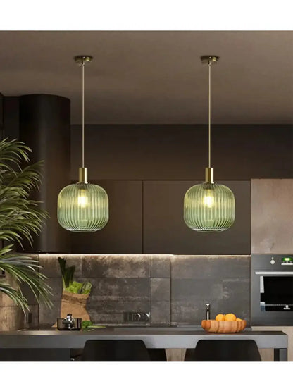 Two elegant green ribbed glass pendant lights with brass accents for dining room use hanging from ceiling