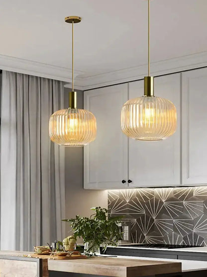 Two elegant gold-finished pendant lights with ribbed glass shades in amber green and grey for dining room use