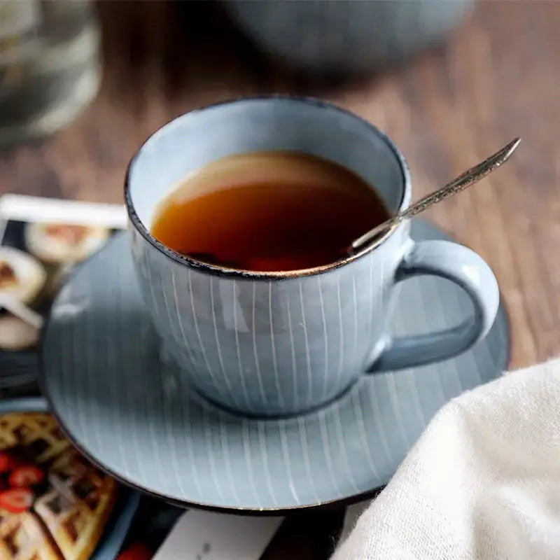 A light blue ribbed matte ceramic coffee cup set with subtle vertical stripes and dark rim resting on matching saucer