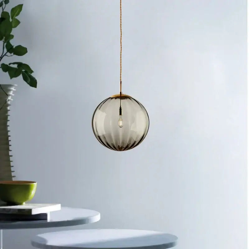 Spherical smoked glass globe pendant light with ribbed texture and brass hardware hanging from braided cord iron finish