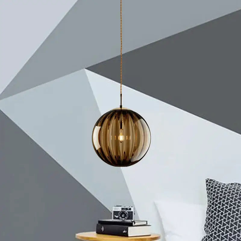 A sleek amber-tinted ribbed glass globe pendant light with iron finish and gold-toned chain for dining room