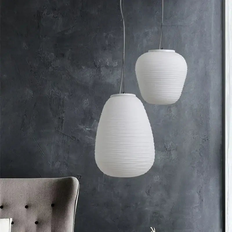 Two white ribbed off-white glass cocoon pendant lights hang against a dark gray wall for dining room decorbites pendant light